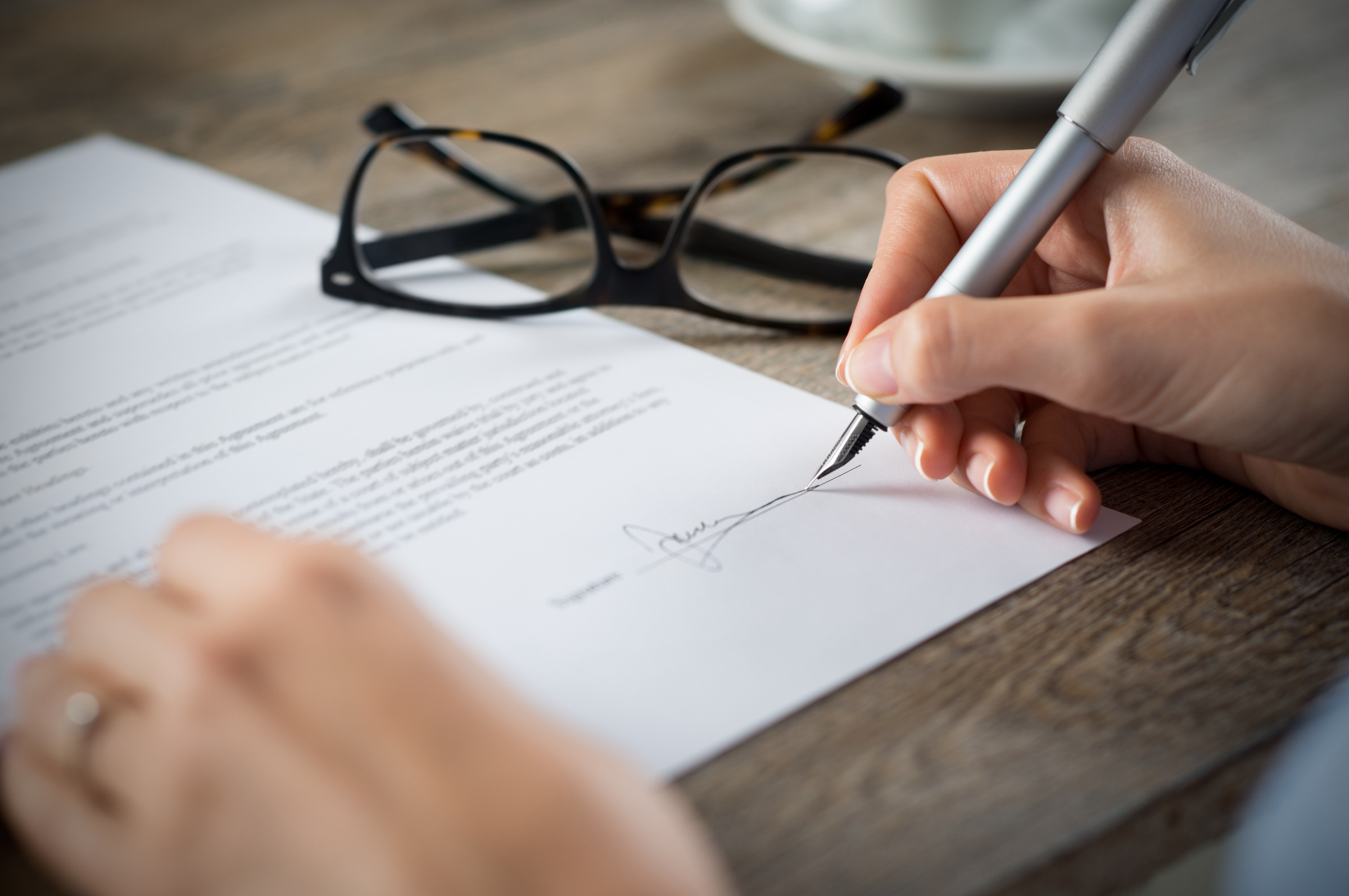 Someone Signing Important Documents on a Wooden Desk