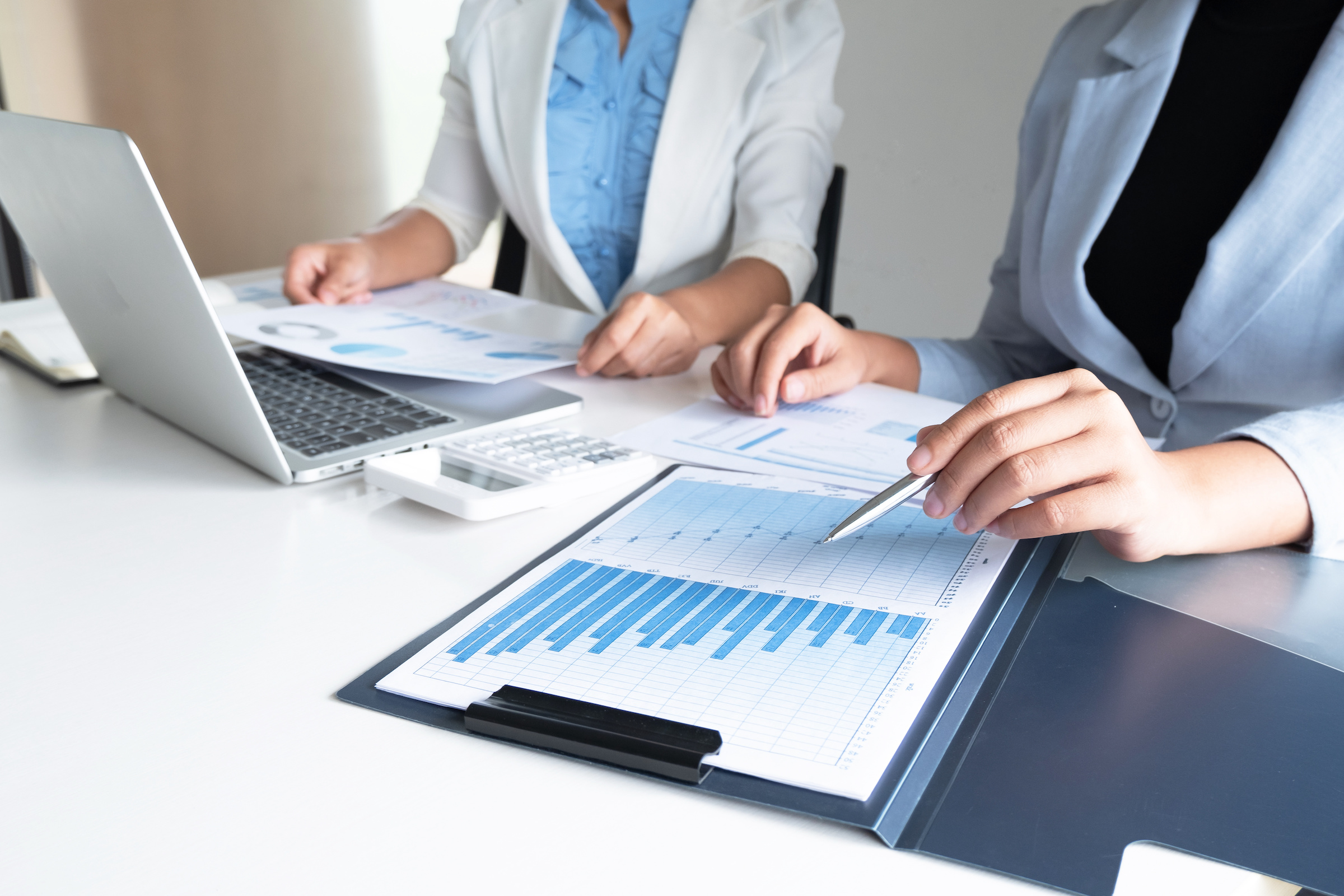 Two People Reviewing Financial Documents on a Table Showing Charts and Graphs